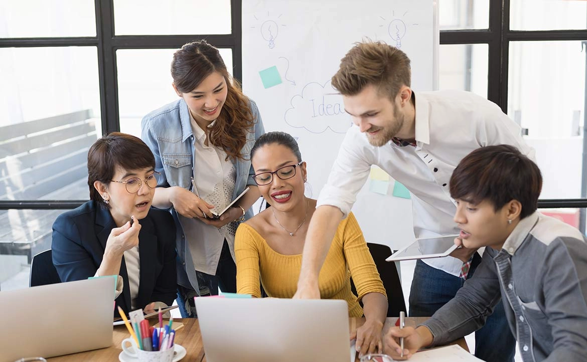 五位同事在辦公室，圍看筆電討論